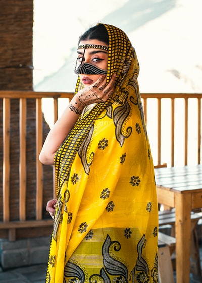 白天站在棕色木栅栏旁的一个戴着黄色和黑色花头巾的女人